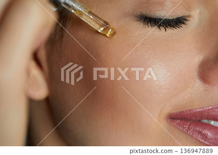 Serum. Moisturisg and nourishing. Close up beauty portrait of beautiful woman with glowing skin is applying a vitamin c skincare product with a pipette dropper.. Serum. Moisturisg and nourishing. Close up beauty portrait of beautiful woman with glowing skin is applying a vitamin c skincare product with a pipette dropper.. 136947889