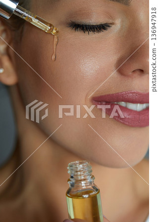 Woman Dropping Serum on Face. Model Girl Applying Serum Collagen Moisturizer from Pipette on Face close up. Positive Laughing Beautiful Woman. Concept of Face Skin Care. 136947918