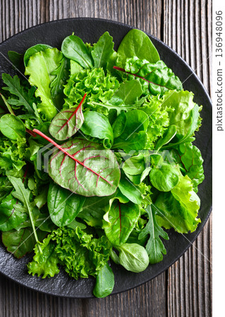 Salad greens with curly lettuce leaves on dark plate 136948096