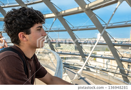 Berlin, germany, august 15, 2023. Young man adminding panoramic berlin skyline from the modern glass dome of the reichstag, contemplating city, light and history 136948281