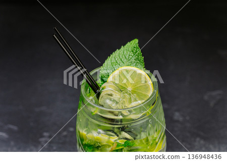 Fresh mojito cocktail with lime, mint and ice in glass on dark background Fresh mojito cocktail with lime, mint and ice in glass on dark background 136948436