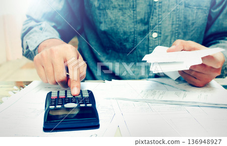 Young asian man using calculator and calculating bills to budgeting and tax calculation monthly expenses. budget management and accounting on table at home. Young asian man using calculator and calculating bills to budgeting and tax calculation monthly expenses. budget management and accounting on table at home. 136948927