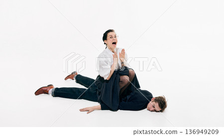 Woman sitting on man lying on studio floor in playful business fashion composition 136949209