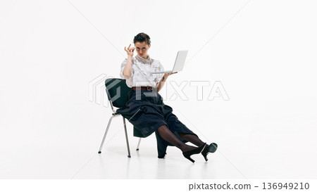 Stylish female professional holding laptop and adjusting glasses in minimal studio. Stylish female professional holding laptop and adjusting glasses in minimal studio. 136949210