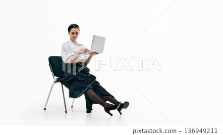 Serious business woman sitting on chair holding laptop and looking confidently at camera 136949211