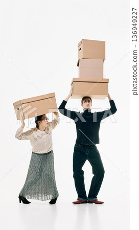 Young couple holding oversized cardboard boxes with expressive reactions on white background Young couple holding oversized cardboard boxes with expressive reactions on white background 136949227