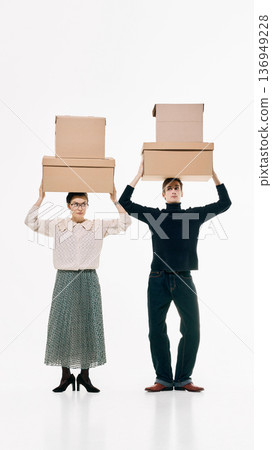 Man and woman in retro outfits holding stacked cardboard boxes on white background 136949228
