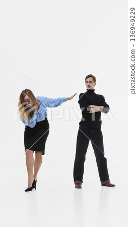 Fashionably dressed woman pushing man away in dramatic studio pose on white background. 136949229