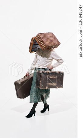 Woman in retro outfit carrying old suitcases with wicker basket covering head on white background Woman in retro outfit carrying old suitcases with wicker basket covering head on white background 136949247