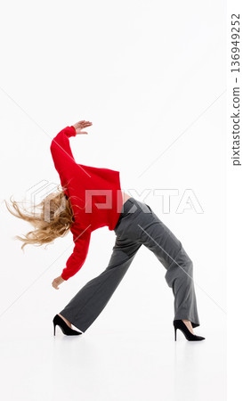 Woman in red sweater and gray trousers bending in dramatic fashion pose on white background. 136949252