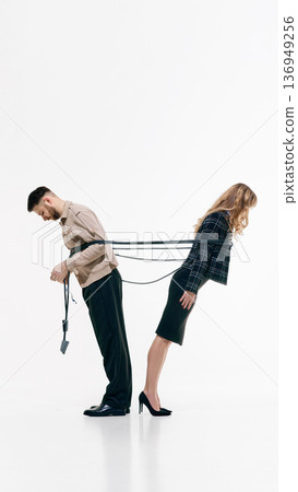 Businessman and businesswoman standing back to back tied together with rope on white studio background Businessman and businesswoman standing back to back tied together with rope on white studio background 136949256