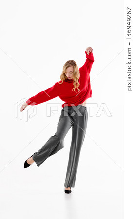 Woman in red sweater, gray trousers and black heels posing in expressive dance movement on white. Woman in red sweater, gray trousers and black heels posing in expressive dance movement on white. 136949267