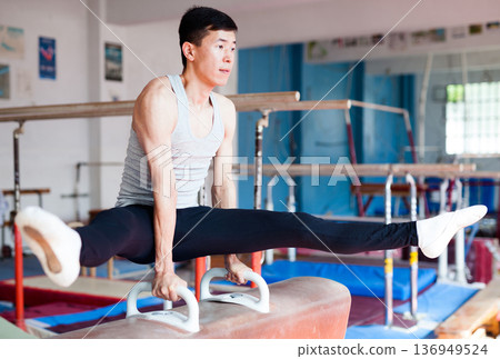 Male gymnast performing exercise on pommel horse Male gymnast performing exercise on pommel horse 136949524