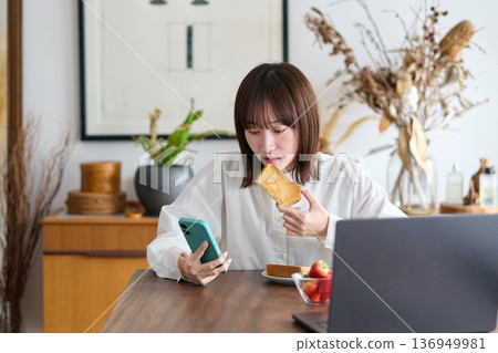 一位女士一邊吃早餐一邊看著她的智慧型手機 136949981