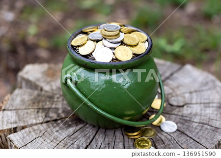 Green Pot Full of Golden and Silver Coins on a Rustic Wooden Stump 136951590