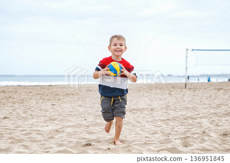 Happy Boy Running on the Beach With a Volleyball During a Cloudy Day Happy Boy Running on the Beach With a Volleyball During a Cloudy Day 136951845