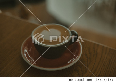 A cup of latte art with a heart shape foam on a wooden table in a cafe. Coffee shop, morning routine, and lifestyle design themes. A cup of latte art with a heart shape foam on a wooden table in a cafe. Coffee shop, morning routine, and lifestyle design themes. 136952135