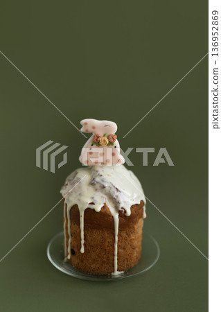 Festive Easter cake with smooth icing and bunny topper on deep green background, elegant holiday composition 136952869