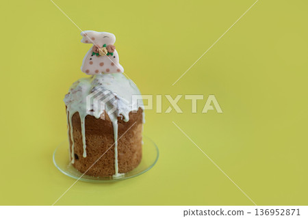 Easter cake decorated with white icing and bunny figurine on bright yellow background, minimal festive composition with copy space Easter cake decorated with white icing and bunny figurine on bright yellow background, minimal festive composition with copy space 136952871