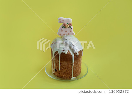 Bright Easter cake topped with white icing and bunny decoration on yellow background, cheerful spring celebration concept 136952872