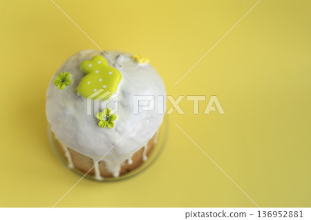 Easter kulich with glossy icing and light green bunny decoration on bright yellow background, cheerful seasonal styling Easter kulich with glossy icing and light green bunny decoration on bright yellow background, cheerful seasonal styling 136952881