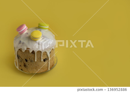 Festive Easter cake decorated with white icing drops and rainbow sugar macarons on vibrant yellow backdrop, seasonal celebration mood 136952886