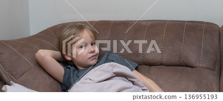 A horizontal shot of a young Caucasian boy relaxing on a brown sofa with his hand behind his head. A horizontal shot of a young Caucasian boy relaxing on a brown sofa with his hand behind his head. 136955193