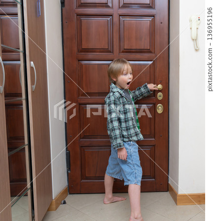 A full-length shot of a young Caucasian boy with blonde hair standing in a home hallway. 136955196
