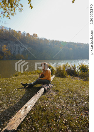 Blonde woman playing string guitar outdoors in autumn forest. Concept of sound therapy, mental health and wellness rituals. Calmness tranquility audio-sensory practices. Aura farming energy Blonde woman playing string guitar outdoors in autumn forest. Concept of sound therapy, mental health and wellness rituals. Calmness tranquility audio-sensory practices. Aura farming energy 136955370