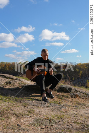 Blonde man playing string guitar outdoors in autumn forest. Concept of sound therapy, mental health and wellness rituals. Calmness tranquility audio-sensory practices. Aura farming energy Blonde man playing string guitar outdoors in autumn forest. Concept of sound therapy, mental health and wellness rituals. Calmness tranquility audio-sensory practices. Aura farming energy 136955371