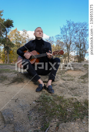 Blonde man playing string guitar outdoors in autumn forest. Concept of sound therapy, mental health and wellness rituals. Calmness tranquility audio-sensory practices. Aura farming energy Blonde man playing string guitar outdoors in autumn forest. Concept of sound therapy, mental health and wellness rituals. Calmness tranquility audio-sensory practices. Aura farming energy 136955375