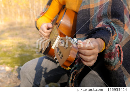 Close up of hands playing string guitar outdoors in autumn forest. Concept of sound therapy, mental health and wellness rituals. Calmness tranquility audio-sensory practices. Aura farming energy 136955424