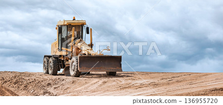 A heavy-duty grader moves soil and shapes the landscape at a construction site, demonstrating the power of engineering against a dramatic backdrop of clouds A heavy-duty grader moves soil and shapes the landscape at a construction site, demonstrating the power of engineering against a dramatic backdrop of clouds 136955720