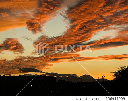 夕陽西下，天空中飄著火紅的雲彩，城市輪廓隱約可見。 136955909