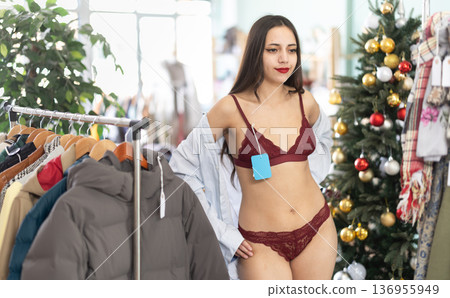Young woman tries on lace lingerie shirt in clothing store Young woman tries on lace lingerie shirt in clothing store 136955949