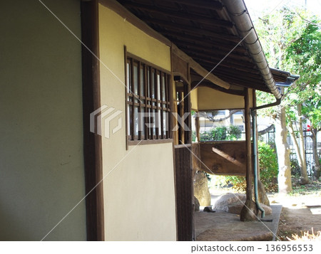 一座日式建築，有格子窗和土牆，還有一條通往花園的走廊。 136956553