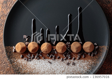 Chocolate truffles on a black plate with chocolate sauce. Chocolate truffles on a black plate with chocolate sauce. 136957016