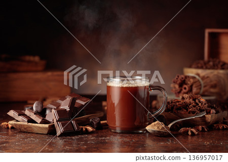 Glass mug of hot chocolate with ingredients on a brown background. 136957017