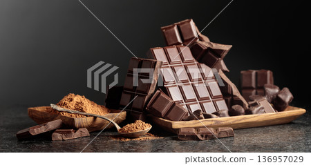Broken dark chocolate bar and cocoa powder on a black background. 136957029