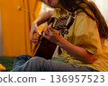 Close up of woman's hands plays guitar at home in her bedroom. She practices music skills on a bed. Creative hobby concept. 136957523