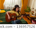 Woman sing and practices guitar at home focusing on musical education and hearing development in a cozy living space with houseplants. 136957526