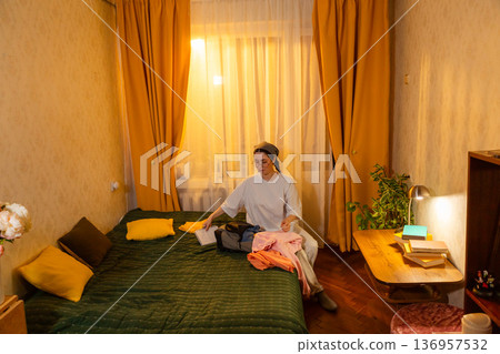 Young Caucasian woman folding laundry indoors in evening light. She creates a tidy room. Home cleaning routine. Wide shot Young Caucasian woman folding laundry indoors in evening light. She creates a tidy room. Home cleaning routine. Wide shot 136957532