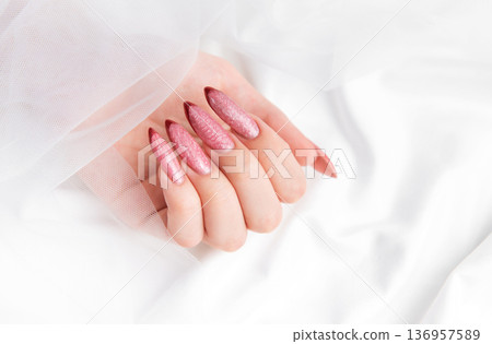 Woman's hand displaying pink shimmering stiletto nails 136957589