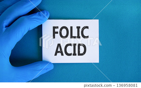Folic acid symbol. Concept words Folic acid on beautiful white card. Doctor's hand in blue medical glove. Beautiful blue background. Medical healthy lifestyle folic acid concept. 136958081