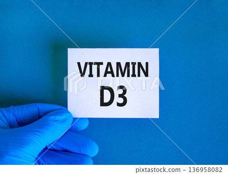 Vitamin D3 symbol. Concept words Vitamin D3 on beautiful white card. Doctor's hand in blue medical glove. Beautiful blue background. Medical healthy lifestyle Vitamin D3 concept. Vitamin D3 symbol. Concept words Vitamin D3 on beautiful white card. Doctor's hand in blue medical glove. Beautiful blue background. Medical healthy lifestyle Vitamin D3 concept. 136958082