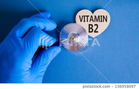 Vitamin B2 riboflavin symbol. Concept words Vitamin B2 on beautiful wooden heart. Doctor's hand blue medical glove. Beautiful blue background. Medical healthy lifestyle Vitamin B2 riboflavin concept. Vitamin B2 riboflavin symbol. Concept words Vitamin B2 on beautiful wooden heart. Doctor's hand blue medical glove. Beautiful blue background. Medical healthy lifestyle Vitamin B2 riboflavin concept. 136958097