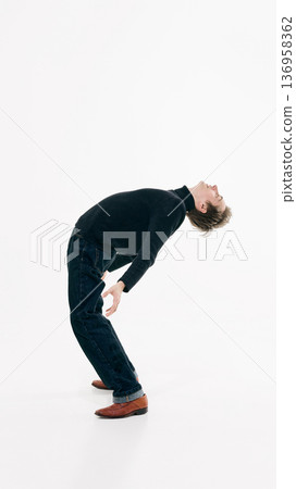 Young man arching backward in expressive pose wearing dark sweater and denim in white studio Young man arching backward in expressive pose wearing dark sweater and denim in white studio 136958362