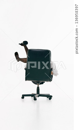 Female figure partially concealed by office chair with raised legs in minimal studio. 136958397