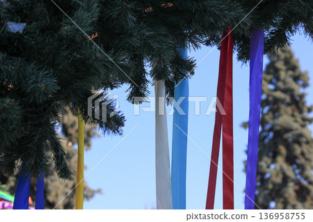 Spring festival decorations with vibrant colorful ribbons on green pine branches against blue sky. Spring festival decorations with vibrant colorful ribbons on green pine branches against blue sky. 136958755