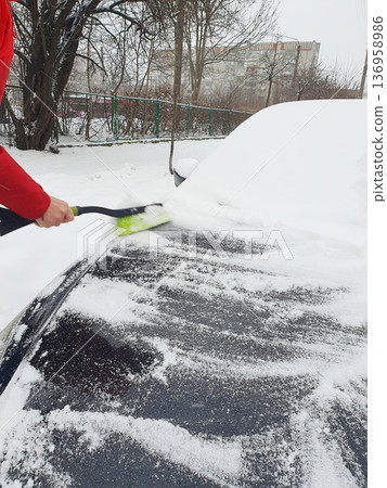 Person brushing fresh snow off black car with green snow brush on cold winter day. Person brushing fresh snow off black car with green snow brush on cold winter day. 136958986